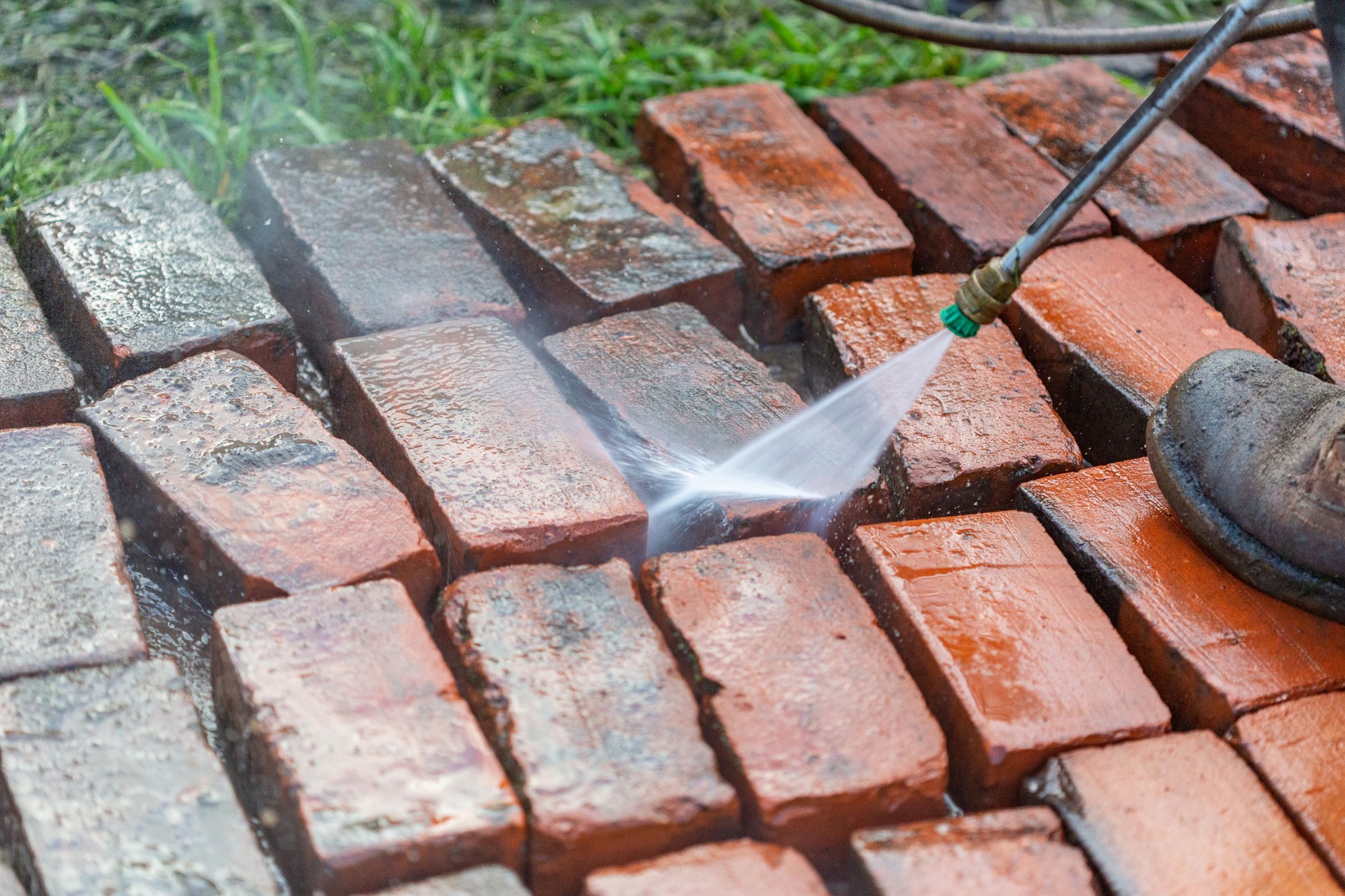 Reclaimed bricks from a fallen chimney being power-washed to be reused for a new patio. Sand in background.